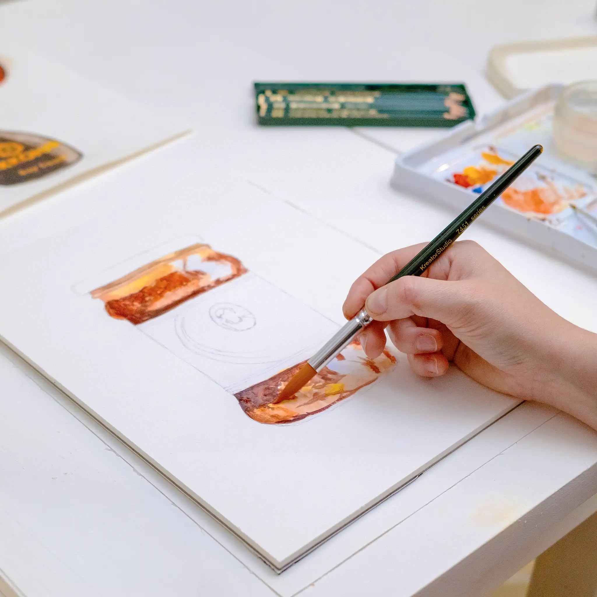 Hand painting a watercolor scene of food on a white surface with a paintbrush.