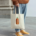 Person holding a tote bag with a sriracha  bottle design, standing on a stone pavement.
